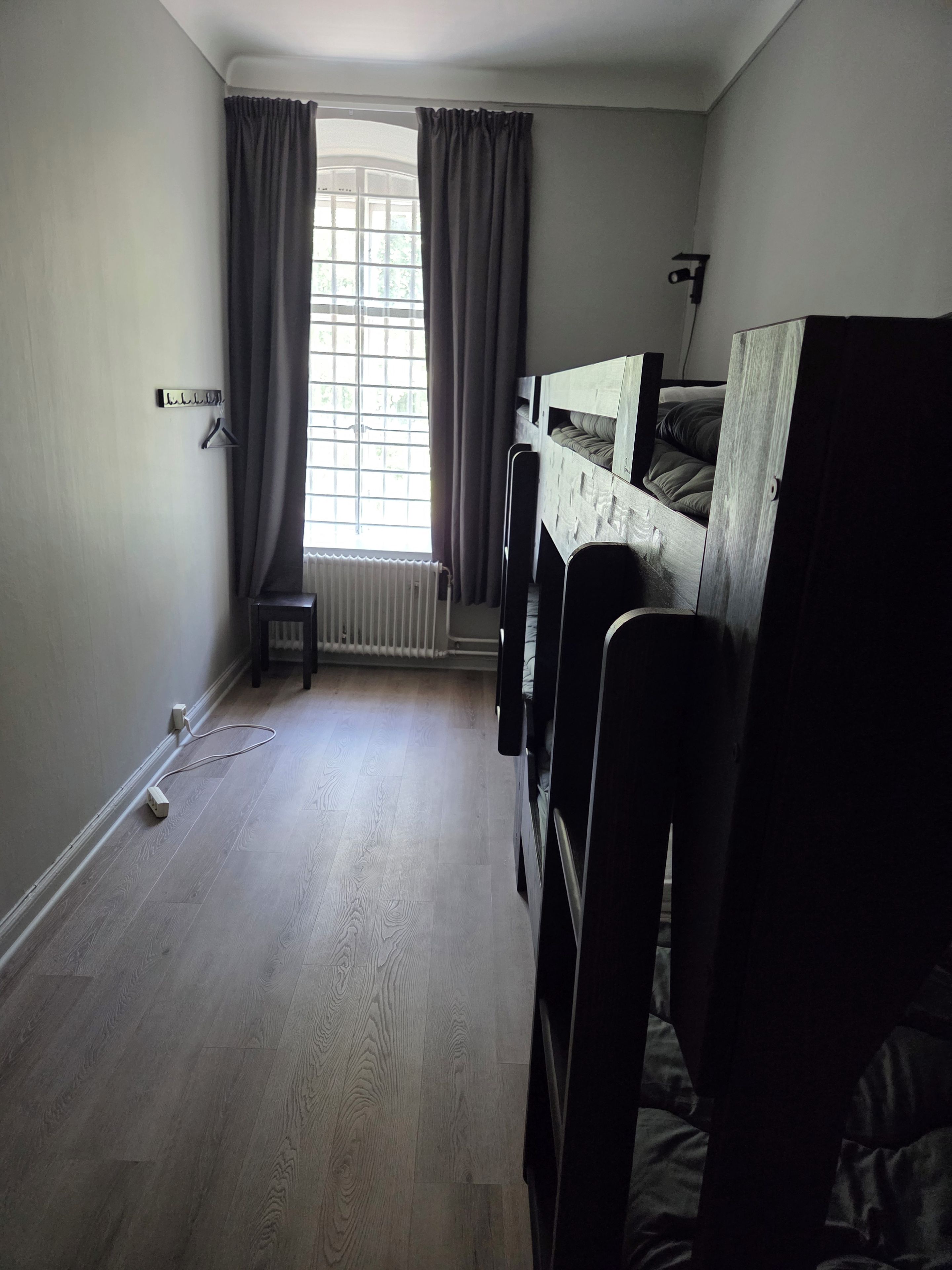 A room with bunk beds, a radiator, a window with curtains, and a power outlet on the floor.