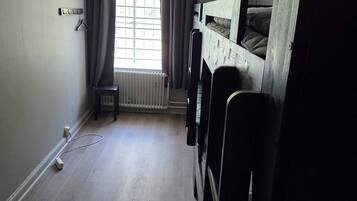 A room with bunk beds, a radiator, a window with curtains, and a power outlet on the floor.