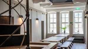 A dining area with wooden tables and benches, large windows, and a staircase. - STF Visby Hamn Vandrarhem (Visby)