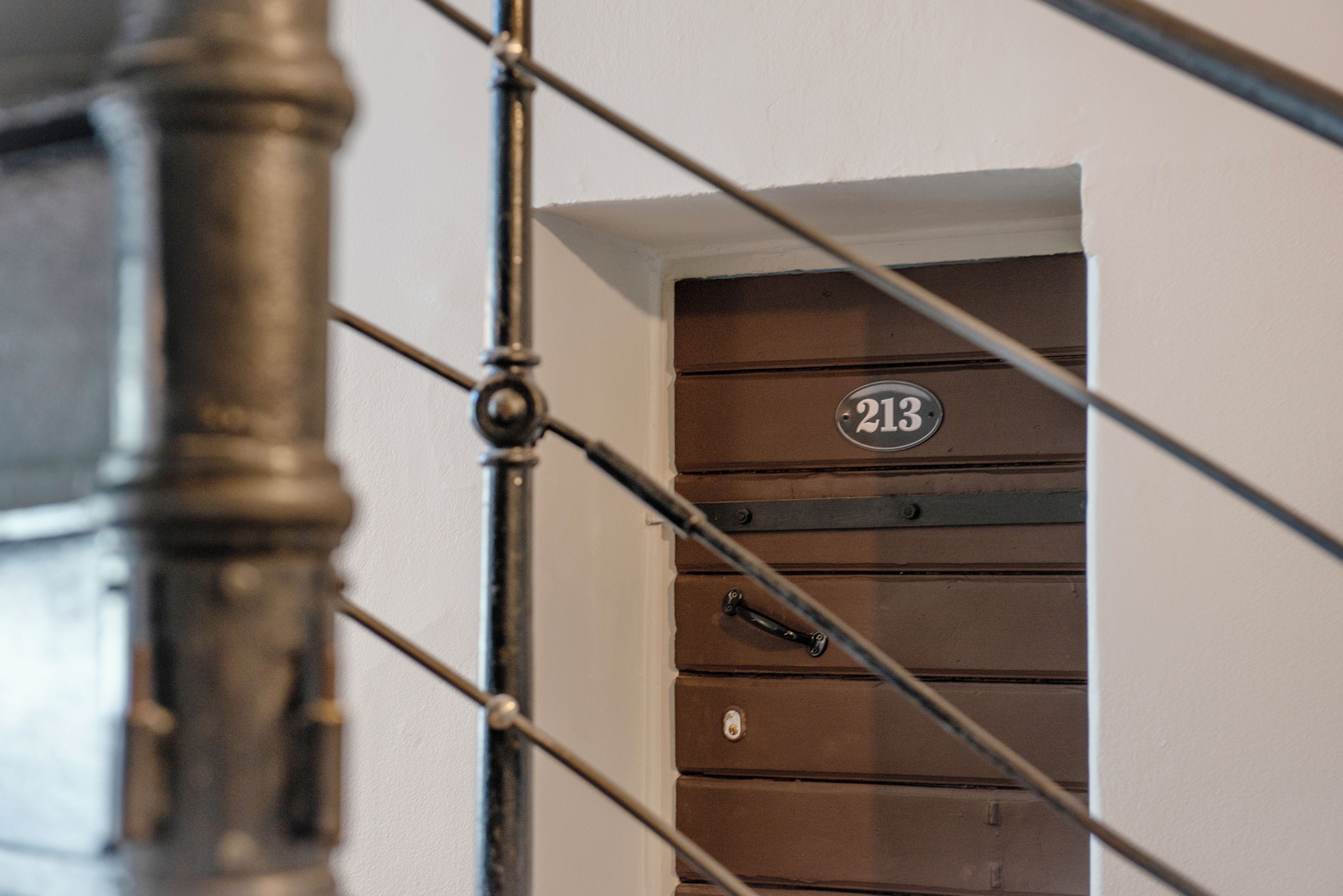 Una escalera con barandilla metálica y una puerta con placa numérica.