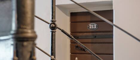 Una escalera con barandilla metálica y una puerta con placa numérica.