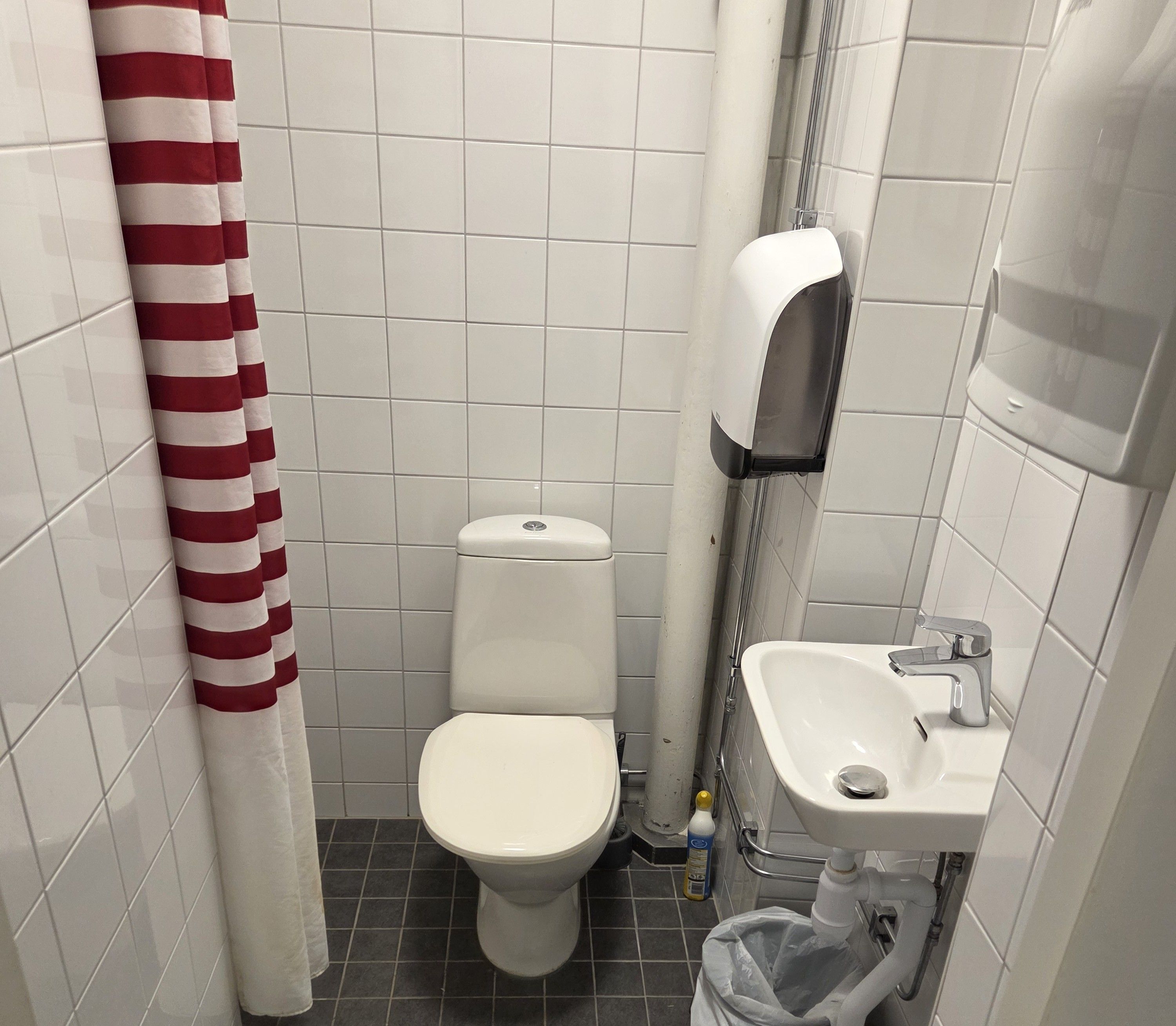 Un baño pequeño con inodoro, lavamanos y secamanos.