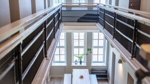 A multi-level interior with a central staircase, metal railings, and a table with a bowl of fruit. - STF Visby Hamn Vandrarhem (Visby)