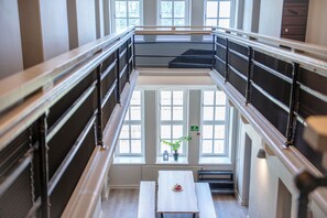A multi-level interior with a central staircase, metal railings, and a table with a bowl of fruit. - STF Visby Hamn Vandrarhem (Visby)