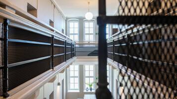 A corridor with a reflective floor, metal railings, and large windows allowing natural light.