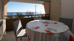 Ein Balkon mit einem Tisch, der mit einer Blumenbettdecke bedeckt ist, Stühlen und Blick aufs Meer.