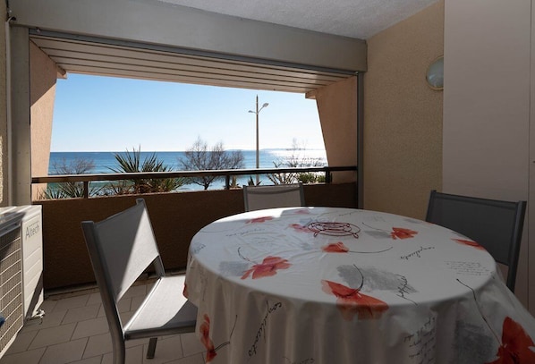 A balcony with a table covered in a floral tablecloth, chairs, and a view of the sea. - Le Lavandou, Studio to rent for 2 people, seaview, steps from the beach (LE LAVANDOU)