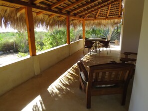 A covered patio with a thatched roof, wooden furniture, and a view of lush greenery. - Villa Gardenia - Casa Cactus by the sea (Todos Santos)
