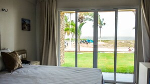 A hotel room with a bed, a nightstand, a lamp, and a view of the beach through large sliding doors. - Locanda Dei Venti (Itarema)