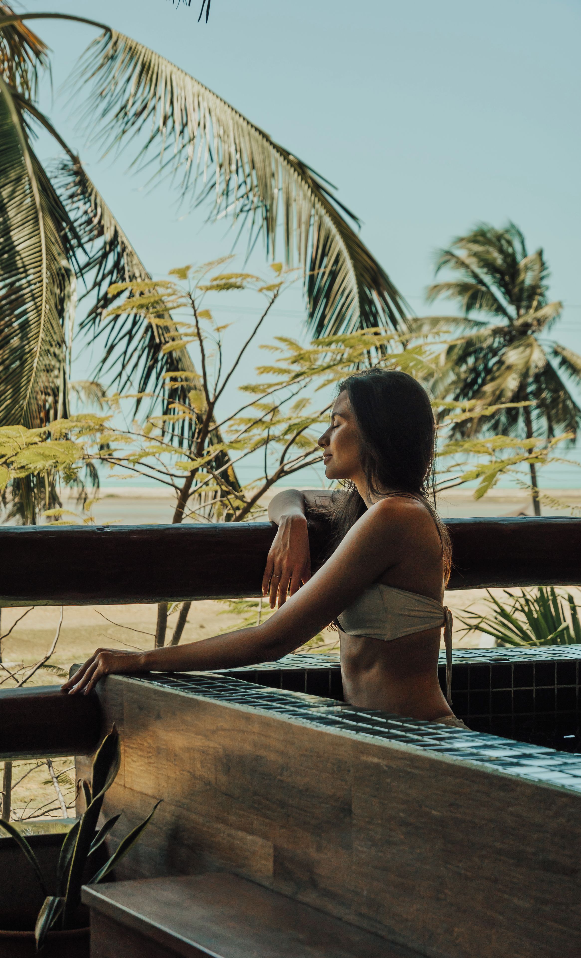 A person sitting by a pool with a view of palm trees and a beach.