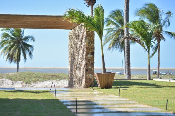A pathway leading to a stone wall with palm trees and a beach in the background. - Locanda Dei Venti (Itarema)