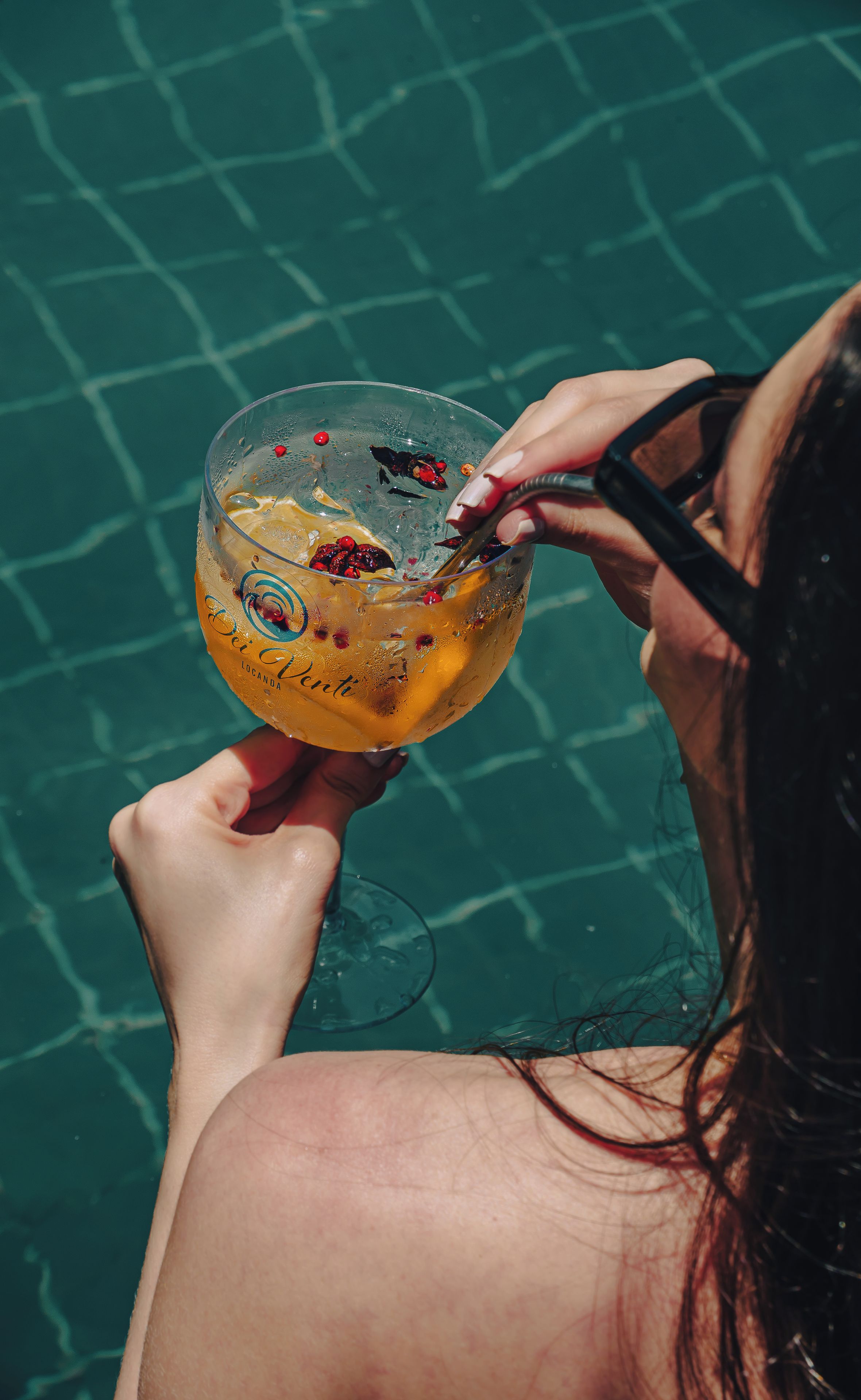 A person holding a glass with a beverage, standing by a pool.