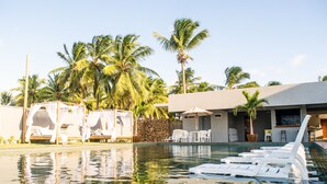 A swimming pool with lounge chairs, a covered seating area, and palm trees in the background. - Locanda Dei Venti (Itarema)