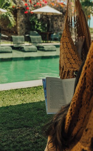 A poolside area with a hammock, lounge chairs, and a book. - Locanda Dei Venti (Itarema)