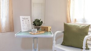 Una pequeña mesa con un cartel de bienvenida, un cactus, una caja y un cojín sobre una silla blanca.