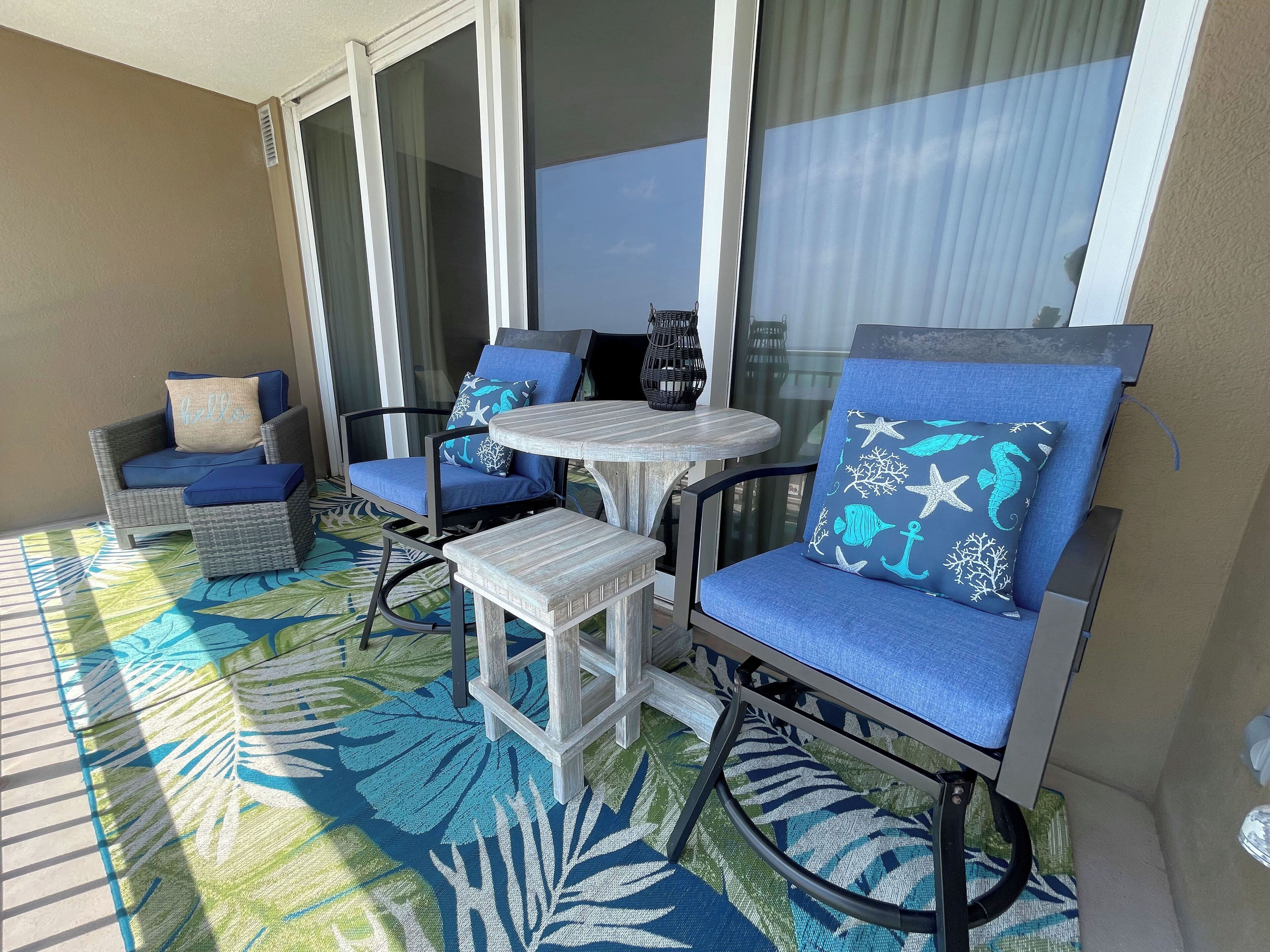Un balcon avec des fauteuils en osier et une petite table, un sol à motifs et une vue sur le ciel à travers les portes vitrées.