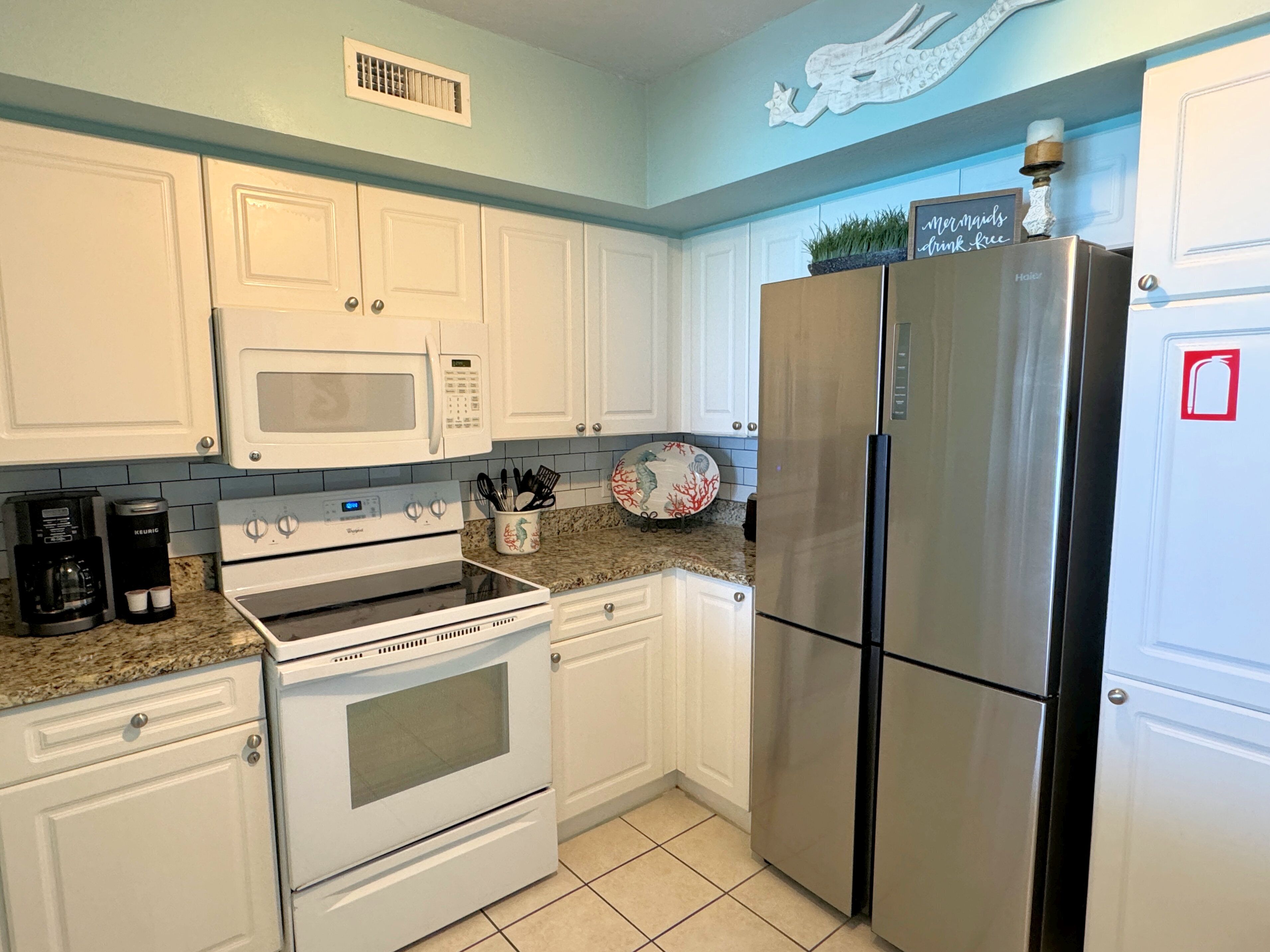 A kitchen with white cabinets, a stainless steel refrigerator, a microwave, and a stove.