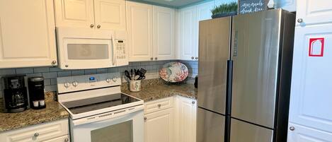 A kitchen with white cabinets, a stainless steel refrigerator, a microwave, and a stove.