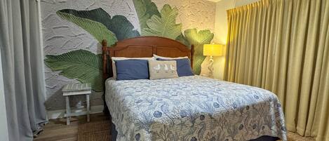 A hotel room with a bed, a ceiling fan, a nightstand, and a wall with a leaf pattern.