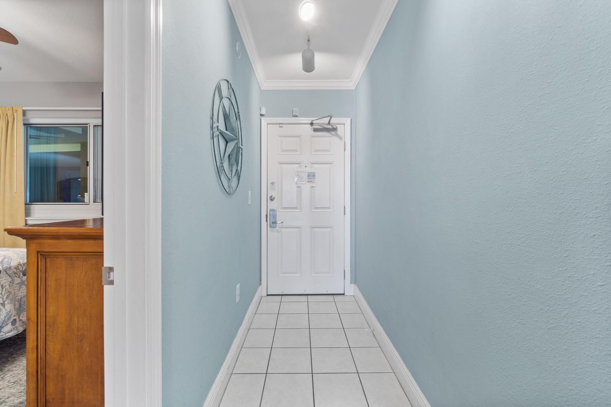 A hallway with a white door, light blue walls, and a ceiling light fixture.