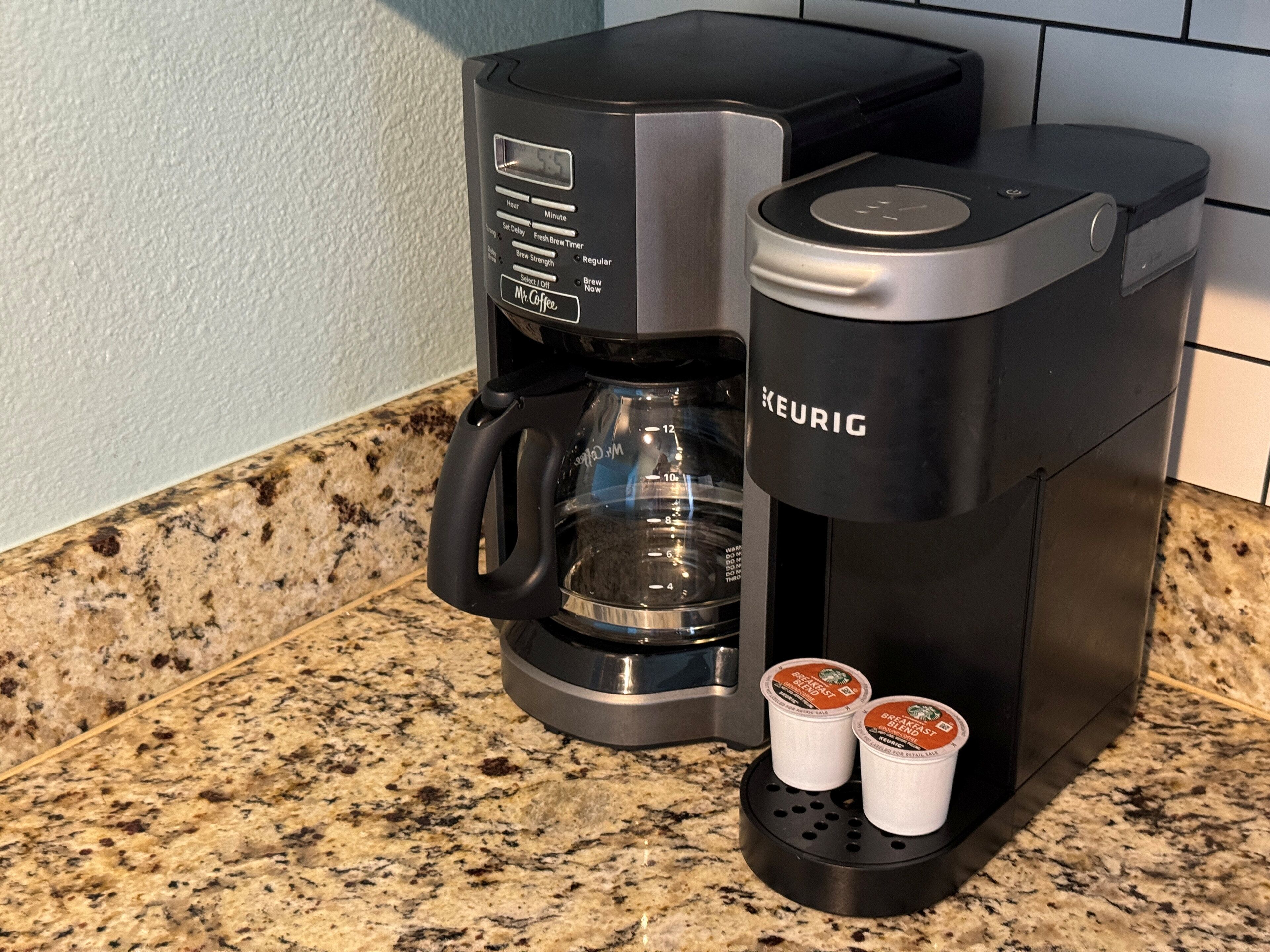A Keurig coffee maker with two coffee pods on its drip tray, placed on a granite countertop.