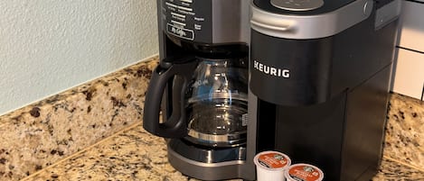 A Keurig coffee maker with two coffee pods on its drip tray, placed on a granite countertop.