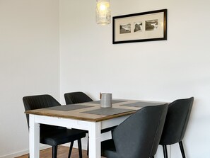 A dining table with four chairs, a candle, and a framed picture on the wall.