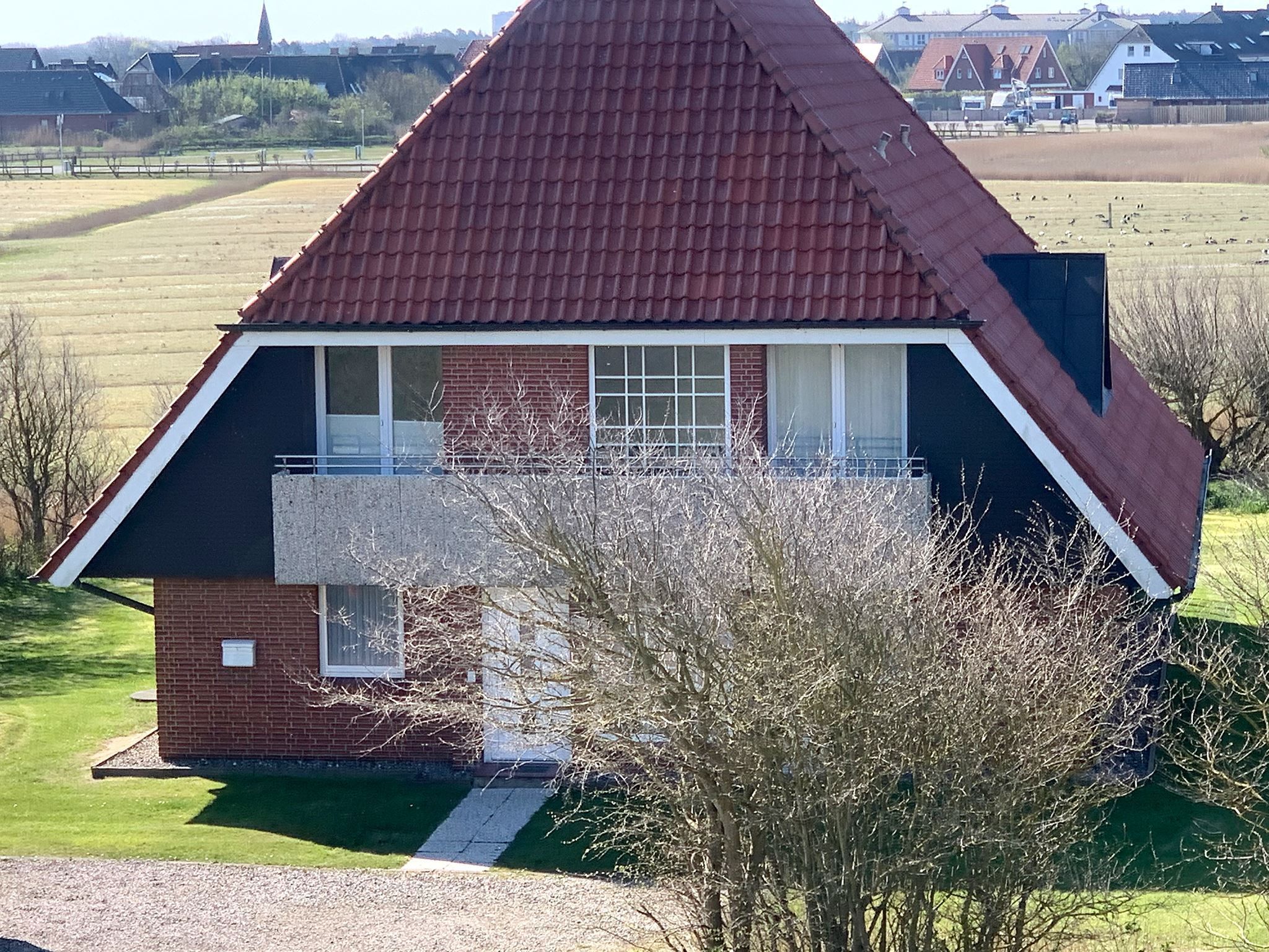Une maison de plain-pied avec un toit rouge, une façade en briques et un petit porche à l’avant.