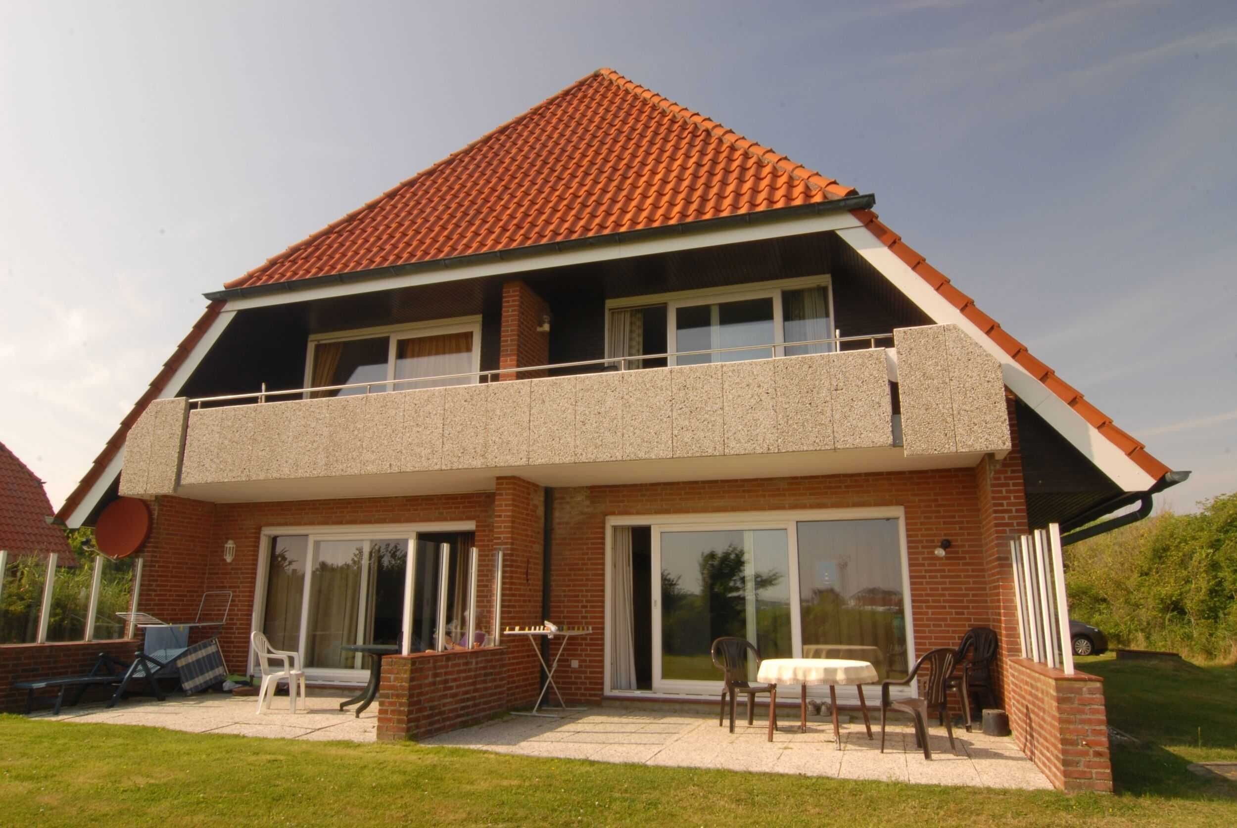 Una casa de dos pisos con balcón, ventanas amplias y un patio con mobiliario exterior.