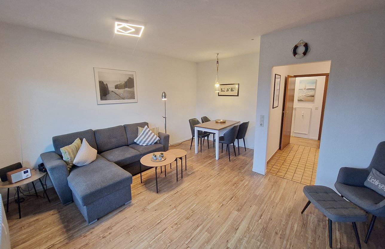 A modern living room with a grey sofa, a coffee table, and a dining area with a table and chairs.