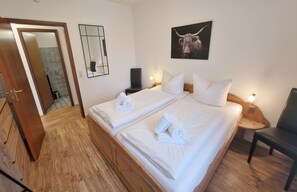 A hotel room with two beds, a wooden floor, a bathroom with a shower, and a bull-themed artwork on the wall.