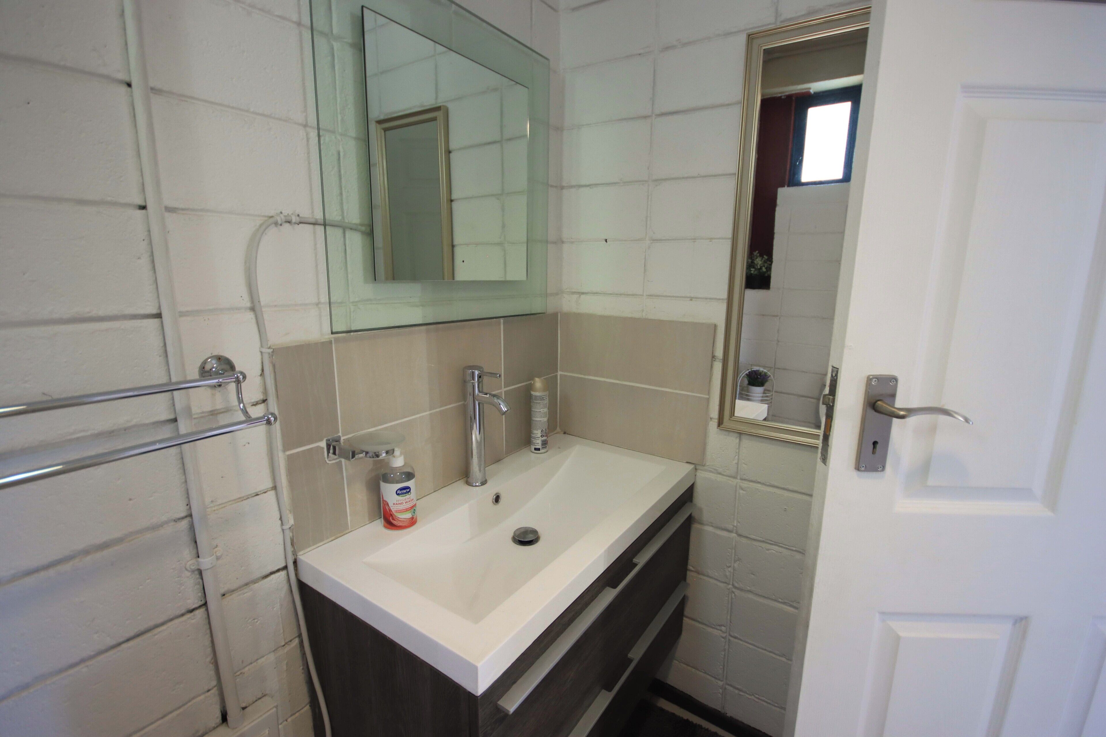 Un baño con lavamanos blanco, un espejo y un perchero para toallas.