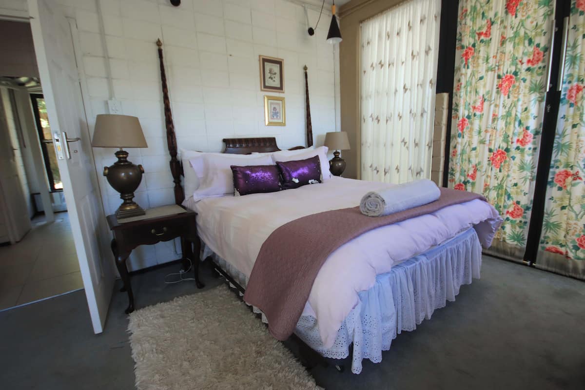 A bedroom with a large bed, two bedside tables with lamps, a wooden headboard, and a floral curtain.