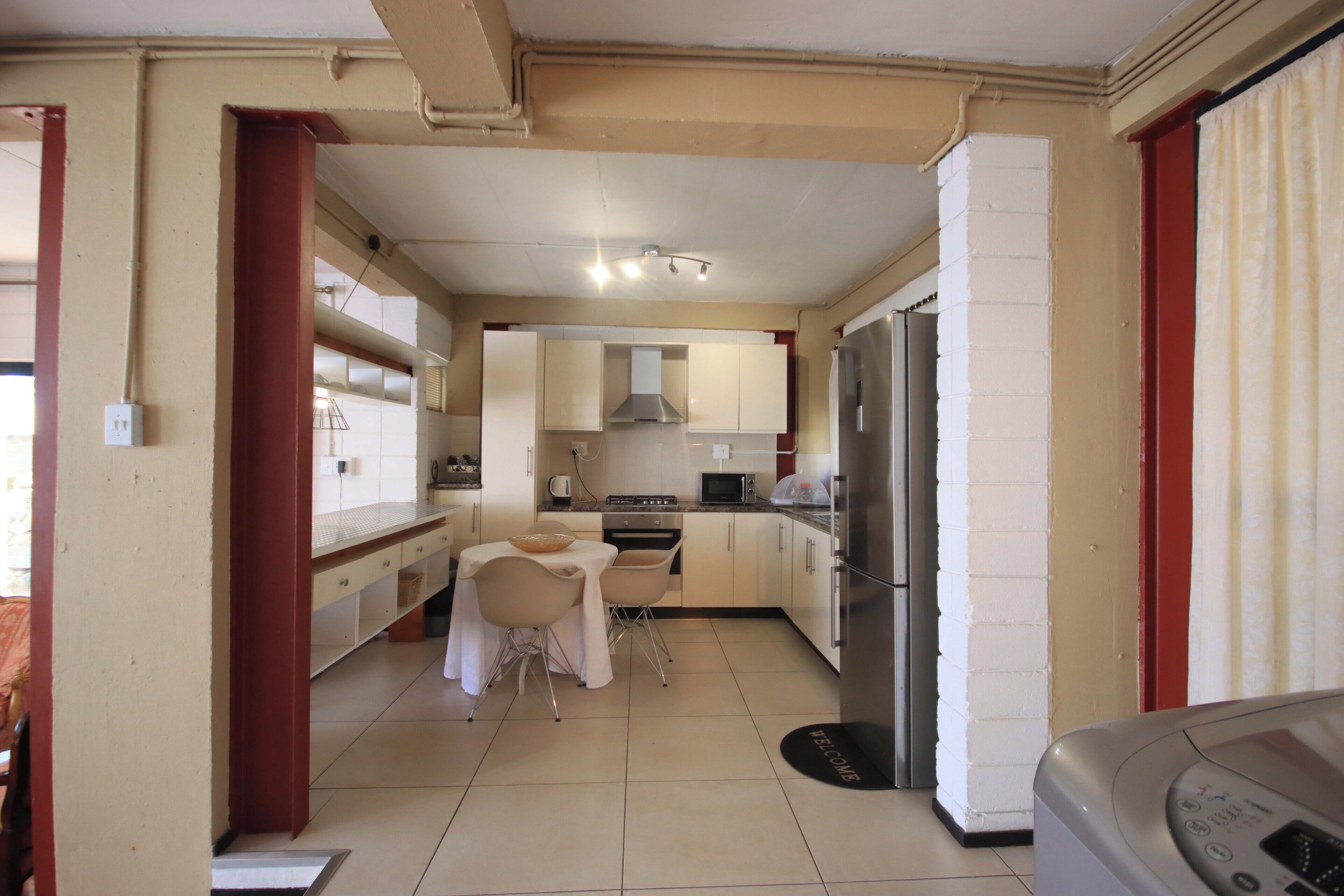 A modern kitchen with white cabinets, a stainless steel refrigerator, and a dining area with a table and chairs.