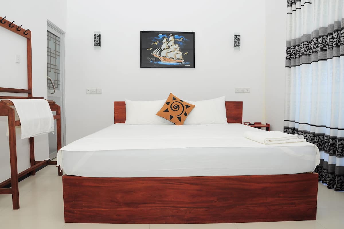 A neatly made bed with a wooden headboard, a single decorative pillow, and a framed picture of a ship on the wall.