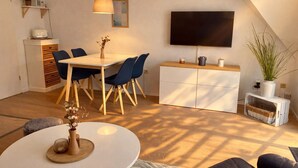 A modern, well-lit room with a dining table, chairs, a TV, and a small cabinet.