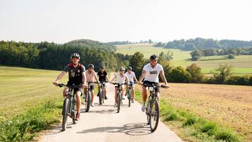 A group of cyclists on a paved path surrounded by greenery and fields.