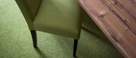 A green upholstered chair with black legs, positioned on a green carpet.