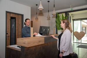 A reception desk with a wooden finish, a computer monitor, and a potted plant.