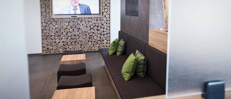 Ein moderner Wartebereich mit Fernseher, Holzverkleidung und Sitzmöbeln mit grünen Kissen.