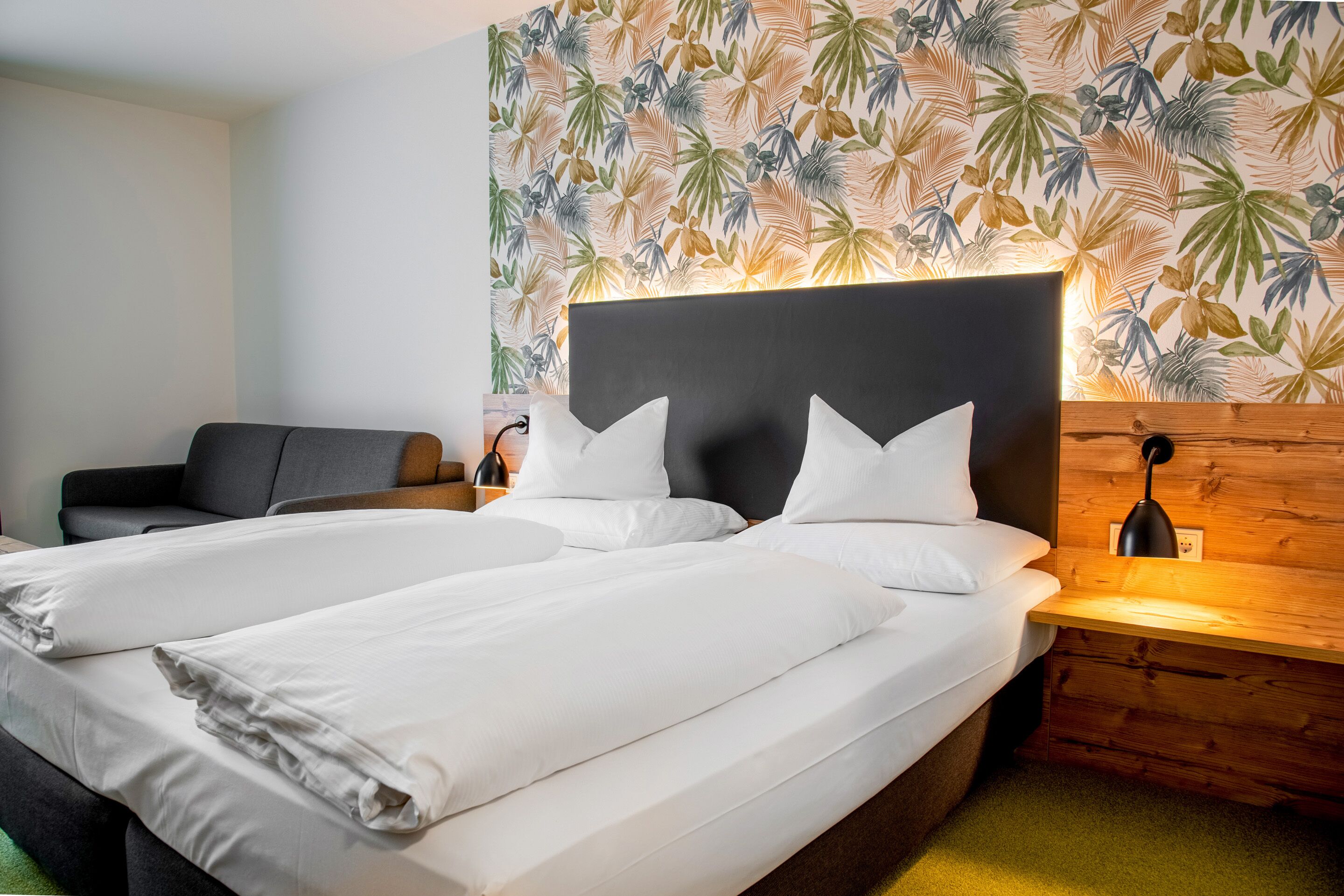 A double bed with white linens, a dark headboard, and a wooden nightstand with a lamp.