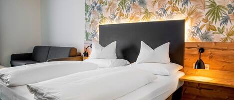 A double bed with white linens, a dark headboard, and a wooden nightstand with a lamp.