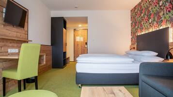 Un hotel moderno con cama, escritorio, silla verde, sofá gris y televisor montado en la pared.