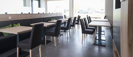 Un restaurante moderno con mobiliario negro y de madera, ventanas amplias y un interior luminoso y cuidado.