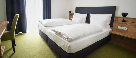 A neatly made bed with white linens, a wooden nightstand with a lamp, and a green carpeted floor.