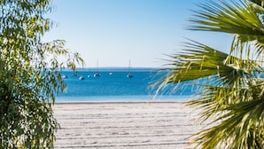 A beach with a clear blue sea, boats, and palm trees. - Apartment Carabela 44 on Alcudia Beach (Alcúdia)