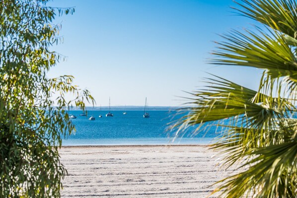 Une plage bordée d’une mer d’un bleu limpide, de bateaux et de palmiers.