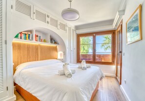 Een slaapkamer met een groot bed, een ingebouwde boekenkast en een raam met uitzicht op palmbomen.