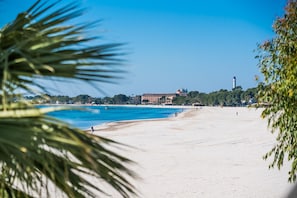 Une plage avec un ciel bleu dégagé, des palmiers et un bâtiment surmonté d’une tour en arrière-plan.