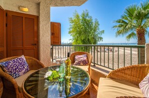 Een balkon met rieten meubels, een glazen tafel en uitzicht op het strand en palmbomen.